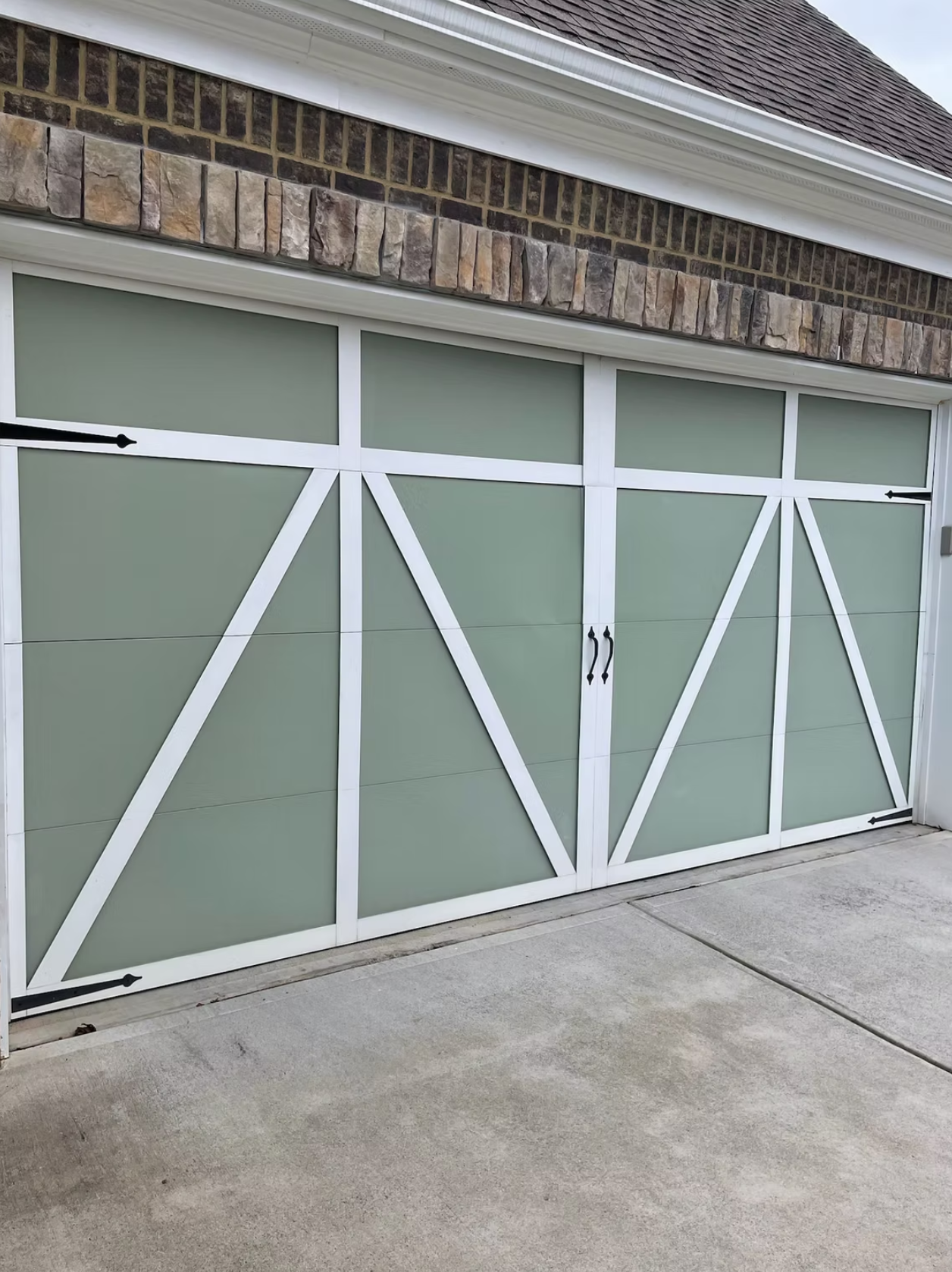 Green and white residential garage door with decorative X-pattern panels and brick details.